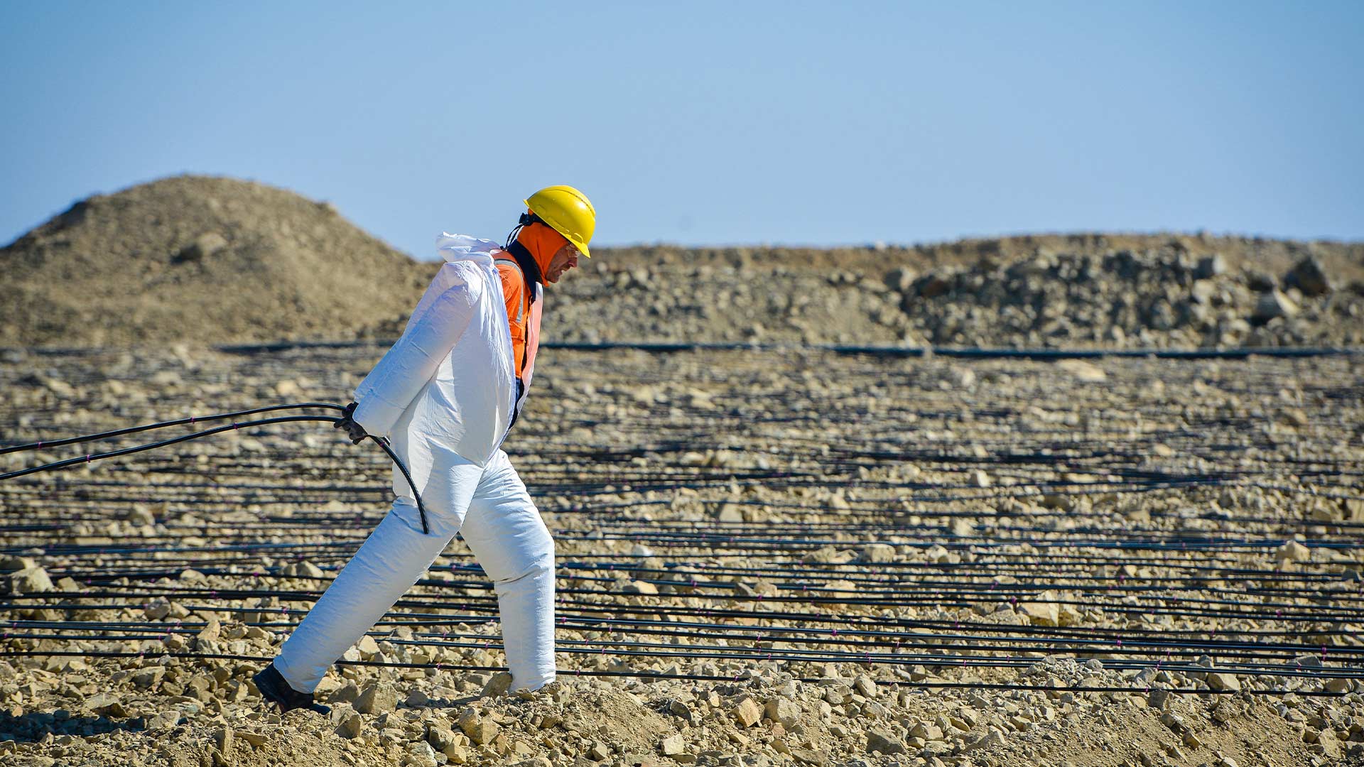 Worker in protective headgear walking along an outdoor rocky environment.