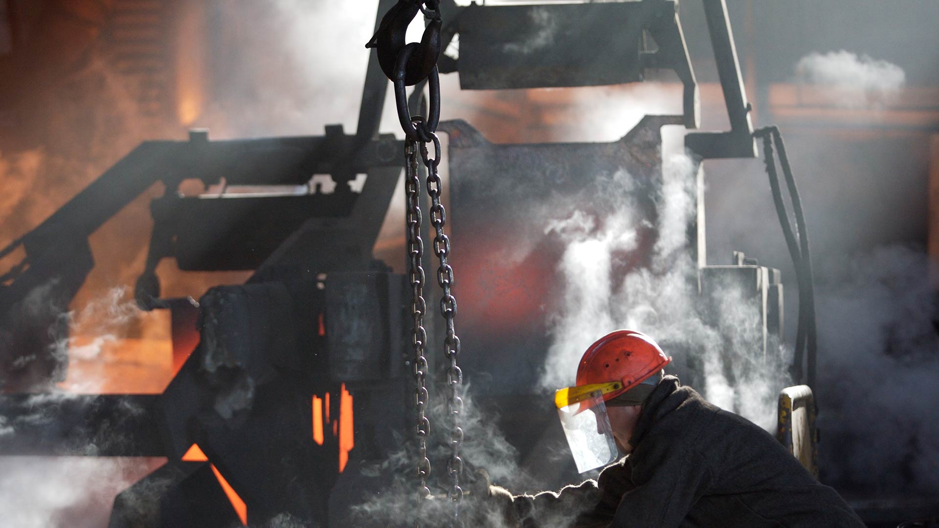 An up-close image of smelting operations. A worker with protective clothes and headgear is seen working in the bottom right. 
