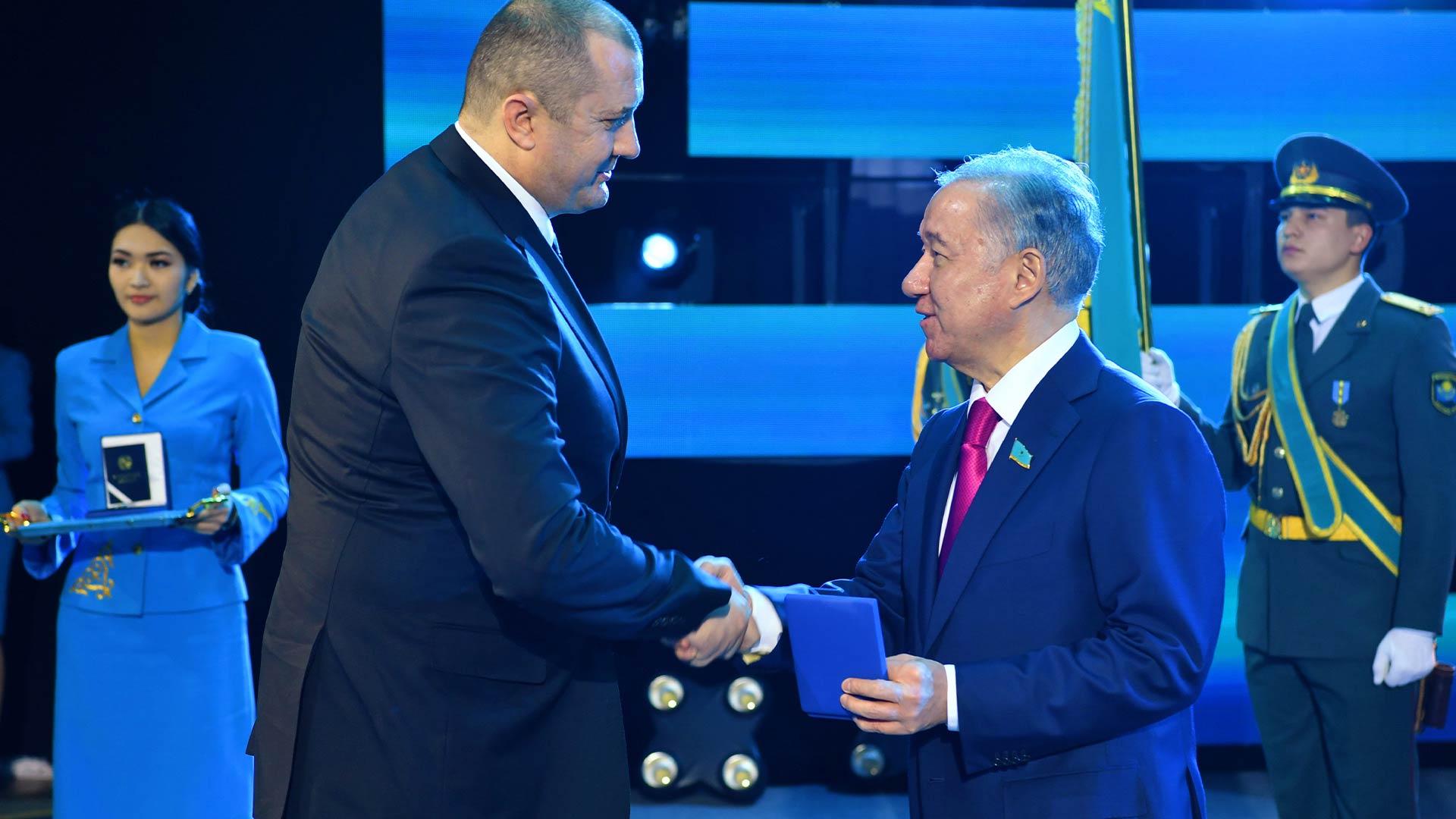Two men in suits shaking hands on stage. 