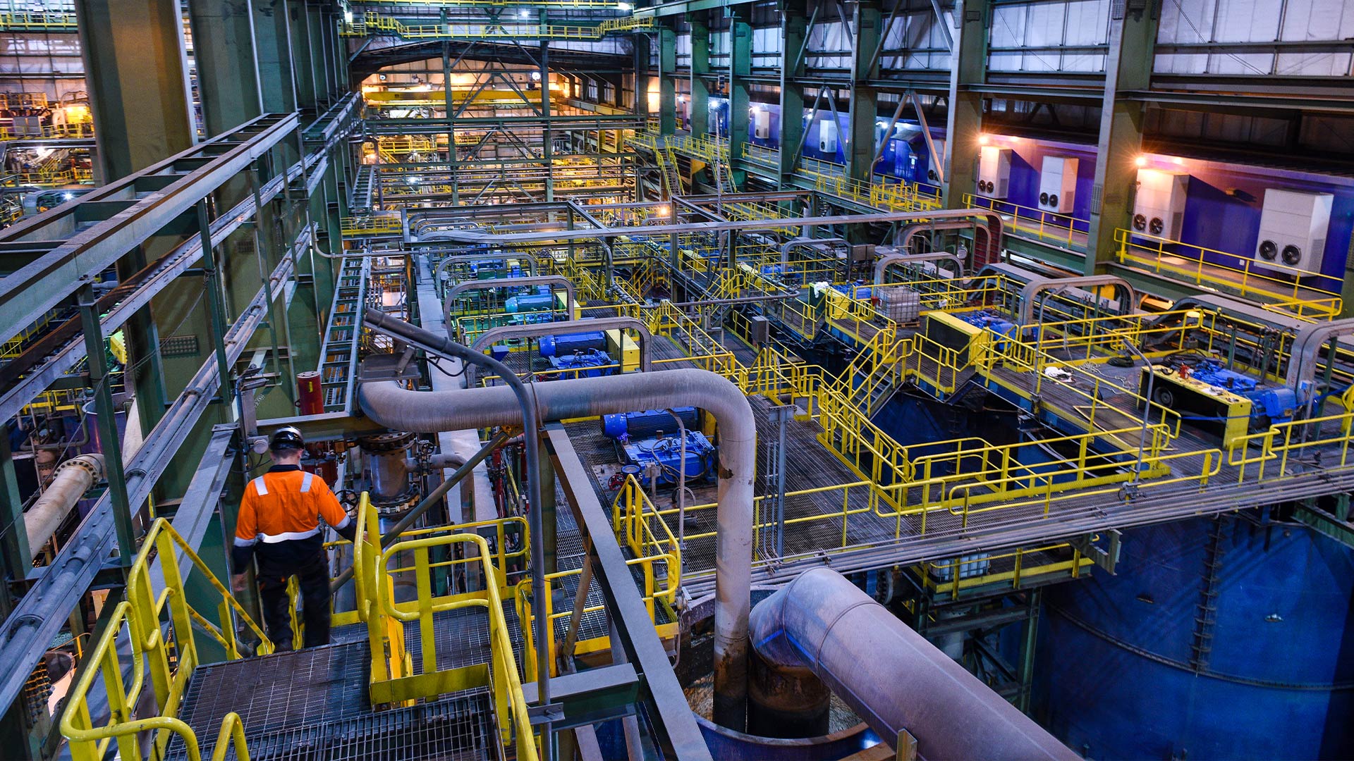 Внутри горнодобывающего предприятия. Слева виден рабочий, спускающийся по лестнице. Видно множество сложных труб и перил, охватывающих обширное пространство.