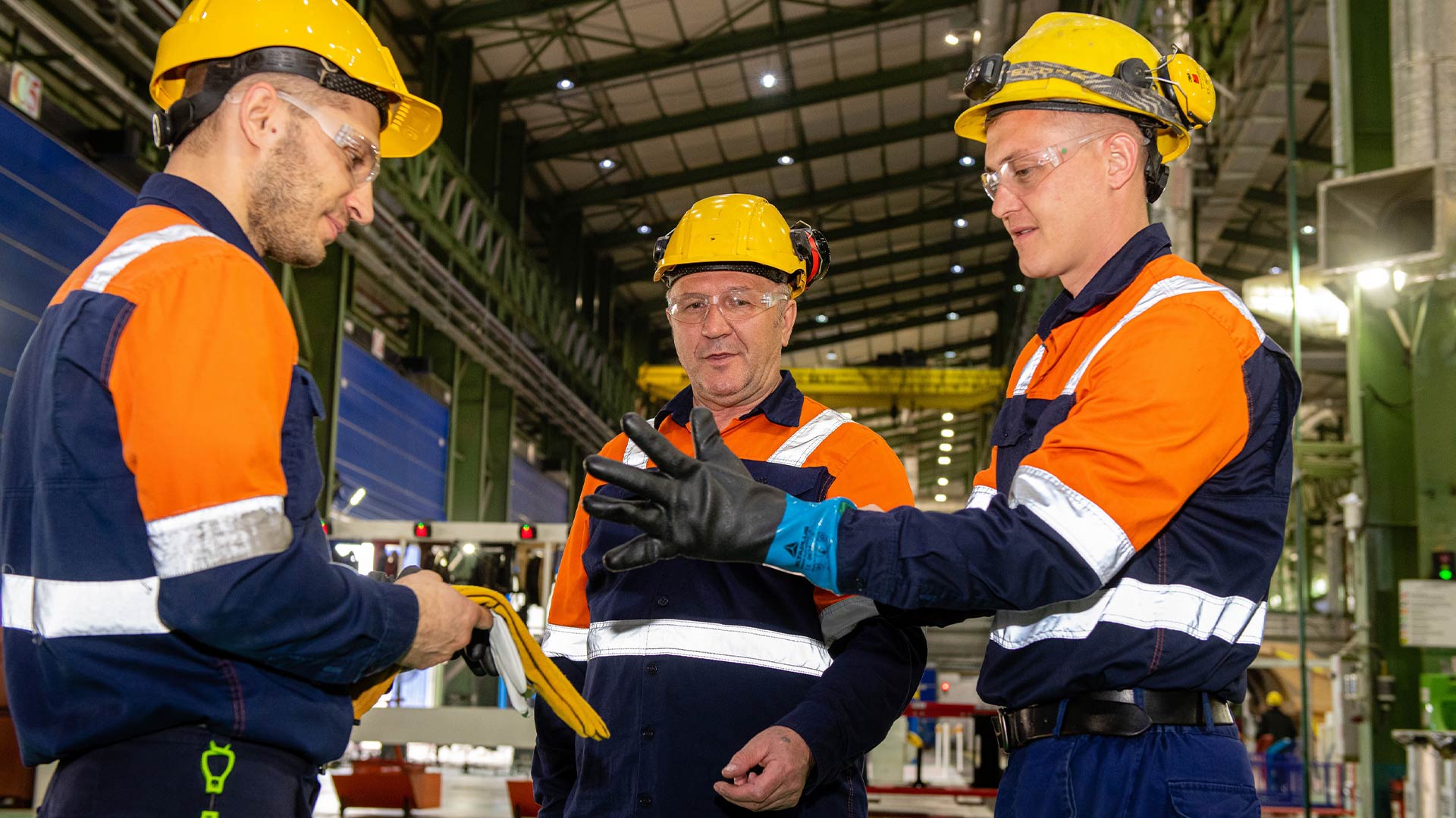 Three workers in safety gear facing each other and having a discussion. 